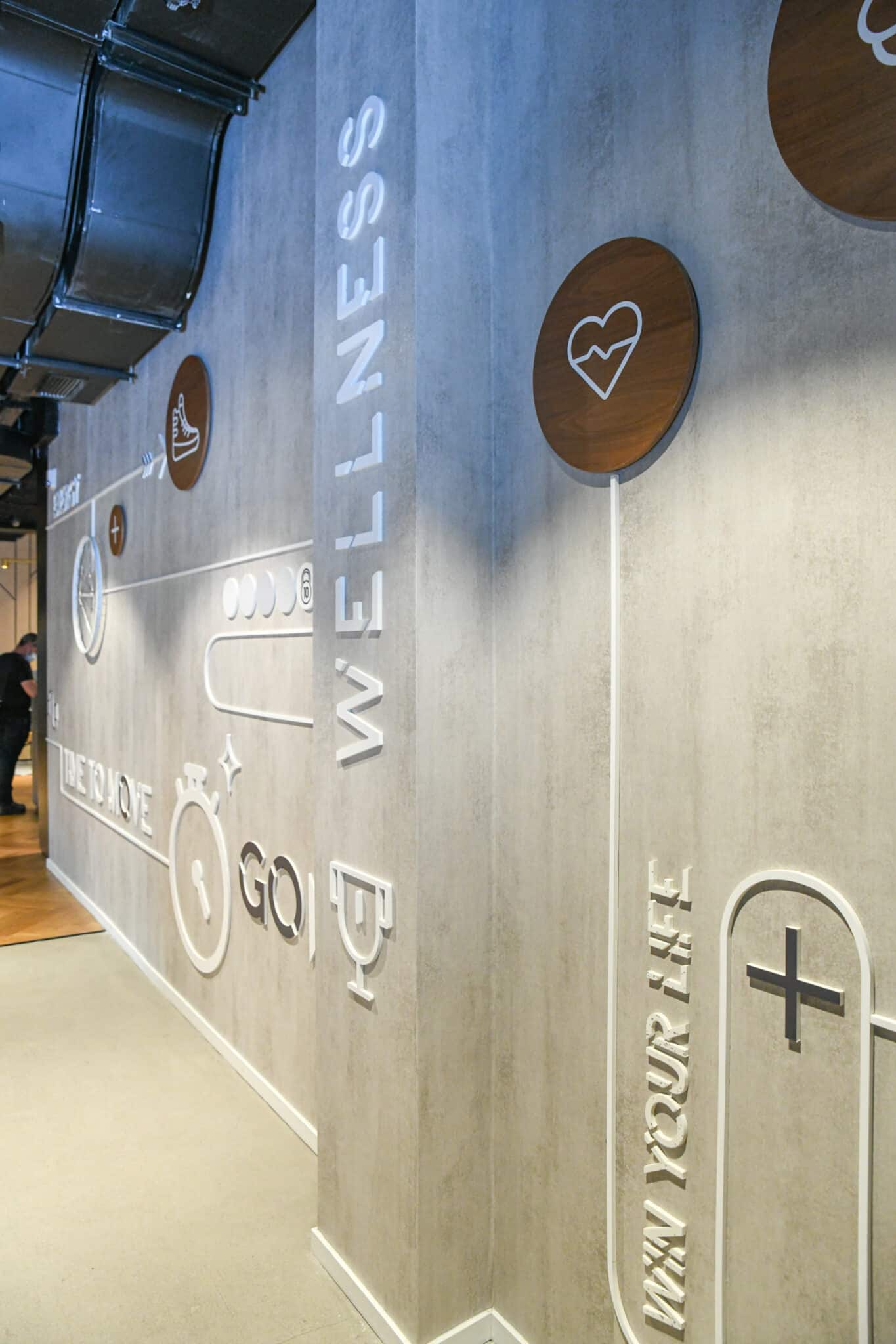 WELLNESS relief lettering with wood discs and icons on a corridor wall