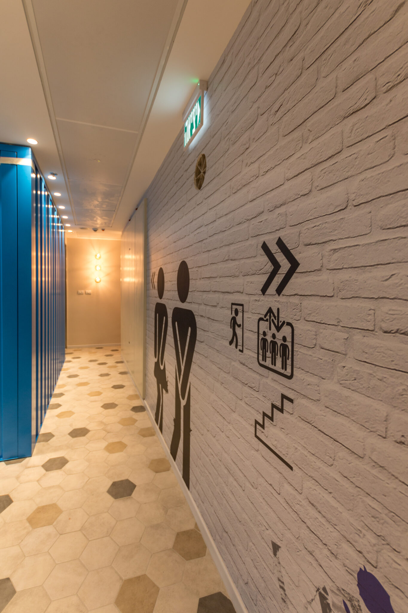 Black pictogram wall graphics on a white brick corridor wall