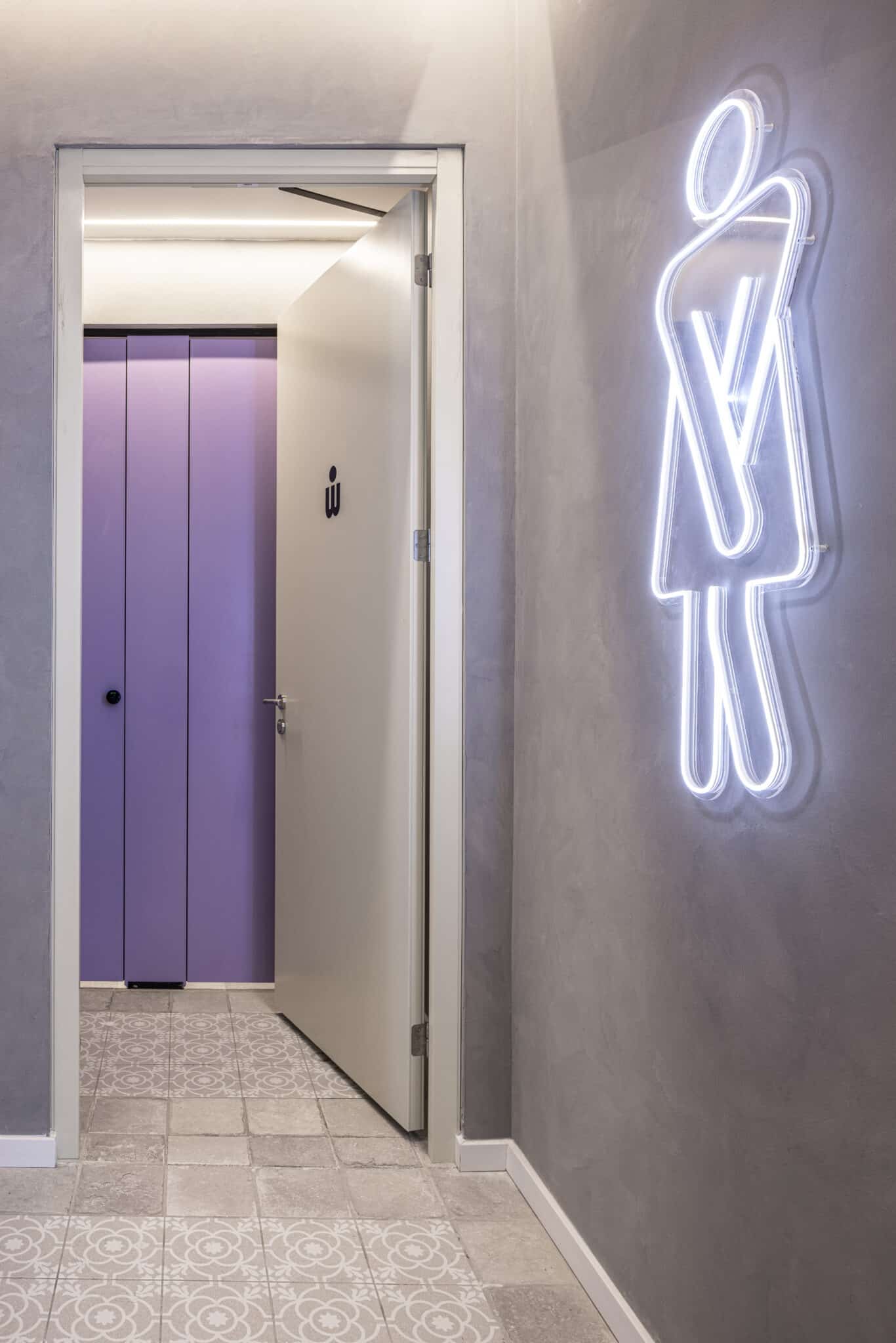 Glowing neon washroom pictogram beside the restroom door