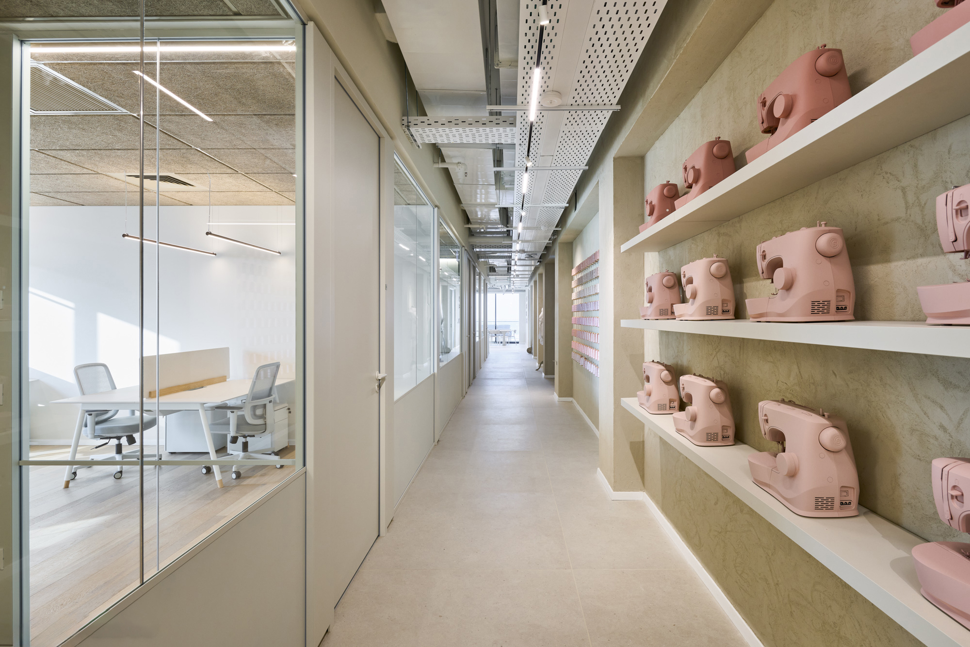 Pink sewing machines on lit display shelves along a corridor