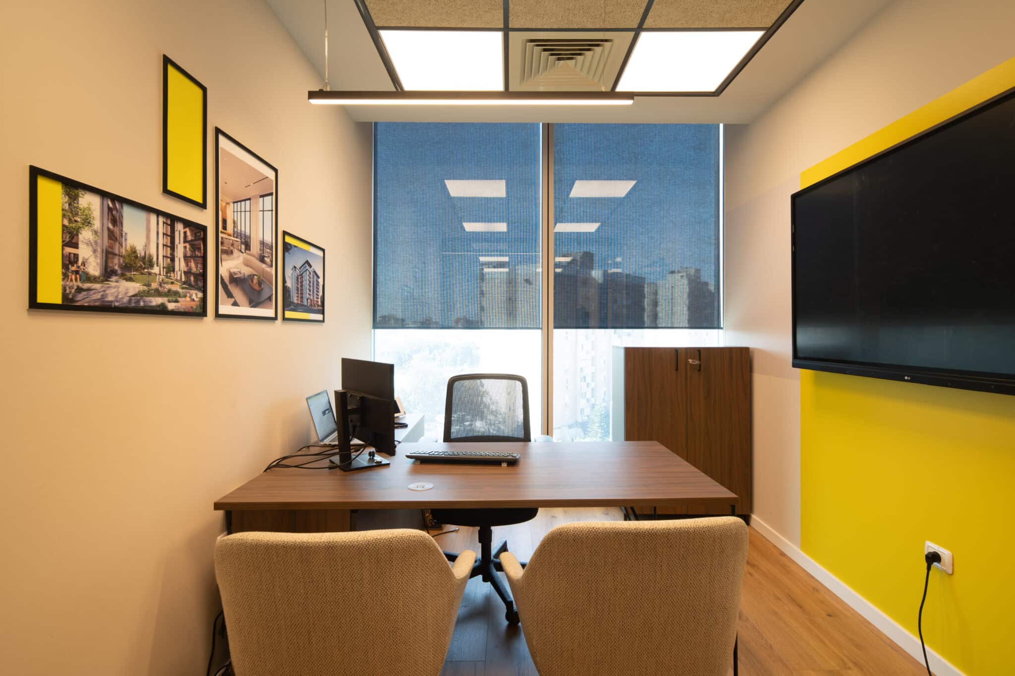 Framed photographs on an office wall beside a yellow accent panel