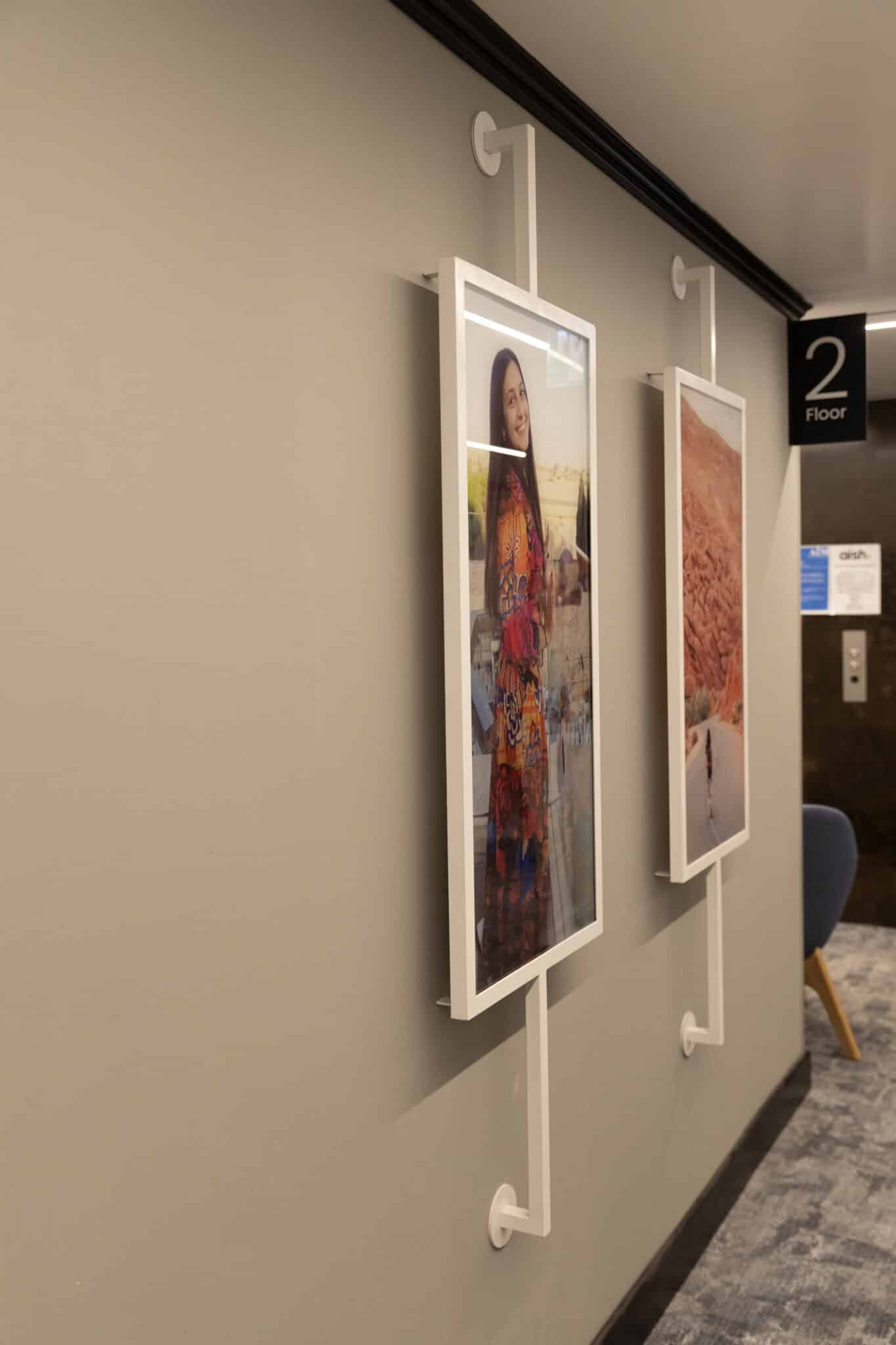Framed photographs suspended on rods beside a floor sign