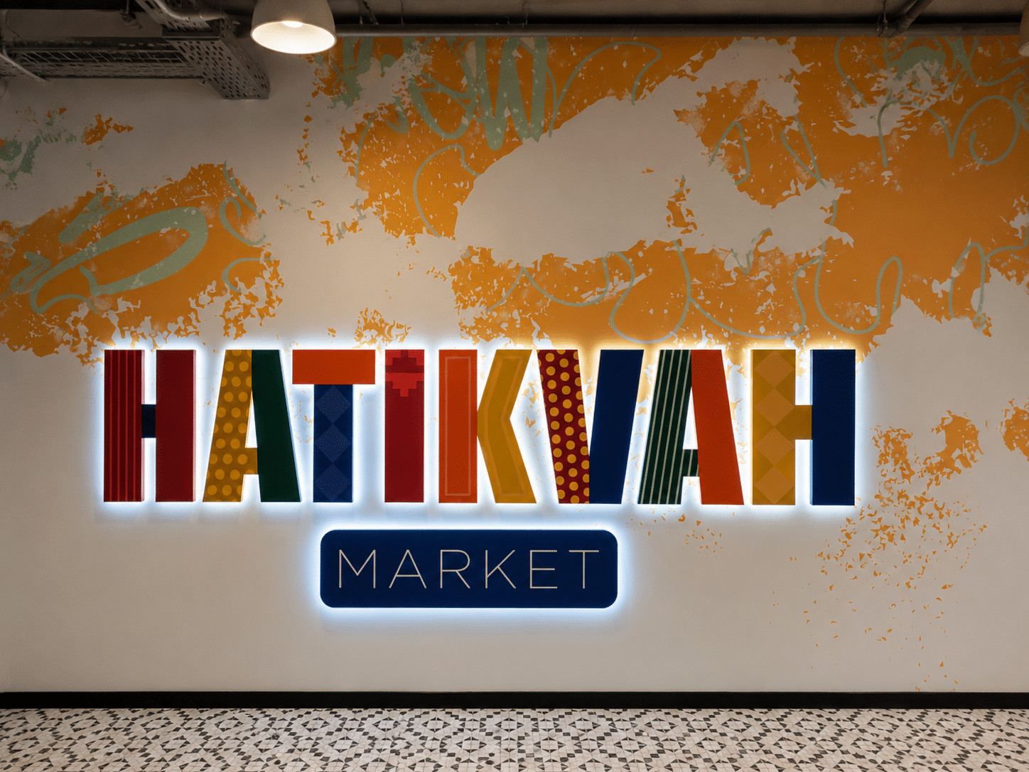 Backlit HATIKVAH MARKET letters filled with colour on a painted wall