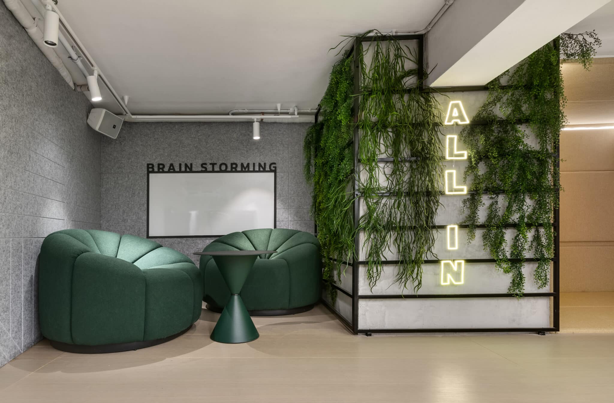 ALL IN neon letters mounted on a plant wall beside a lounge