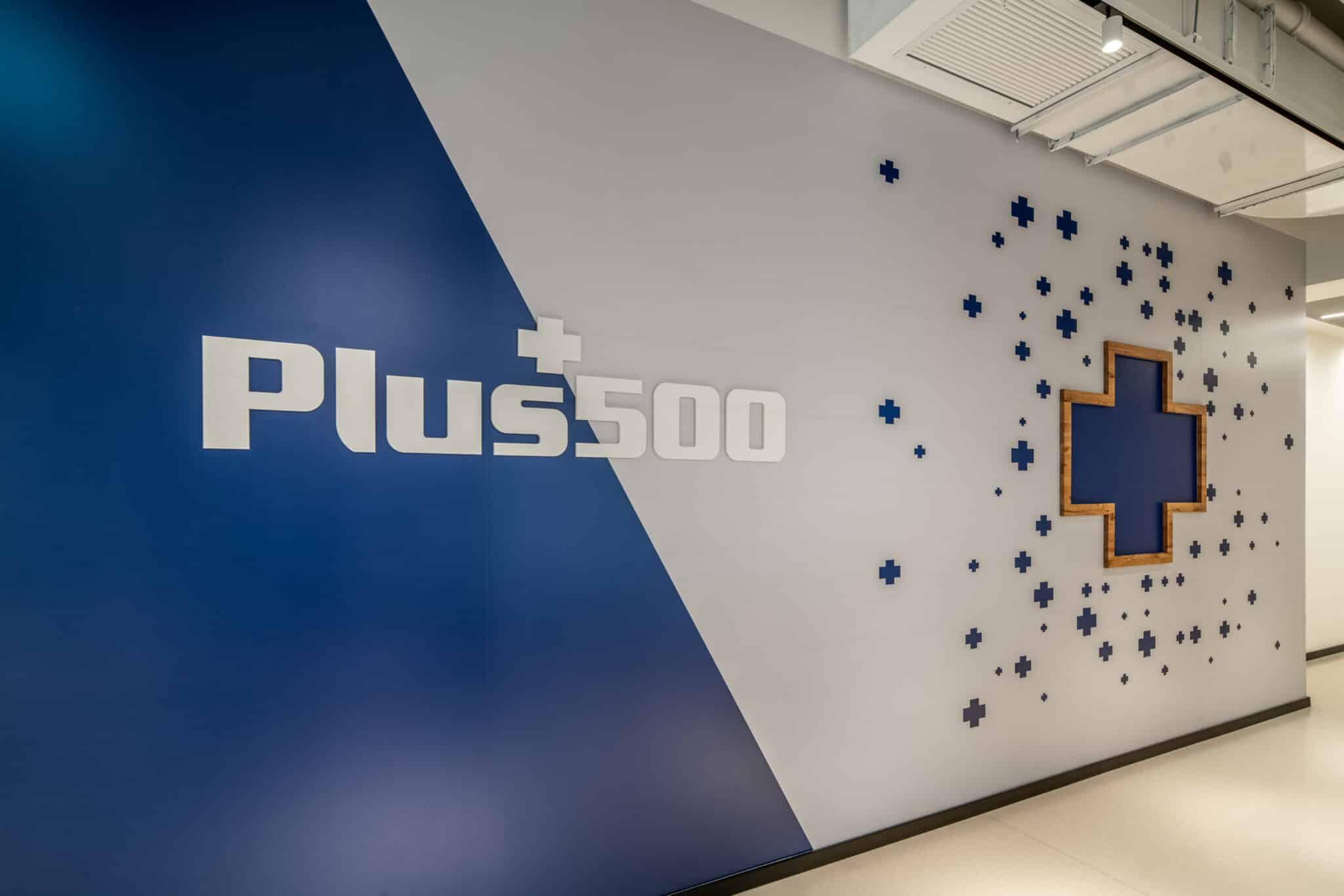 Plus500 logo with scattered 3D crosses on a two tone wall