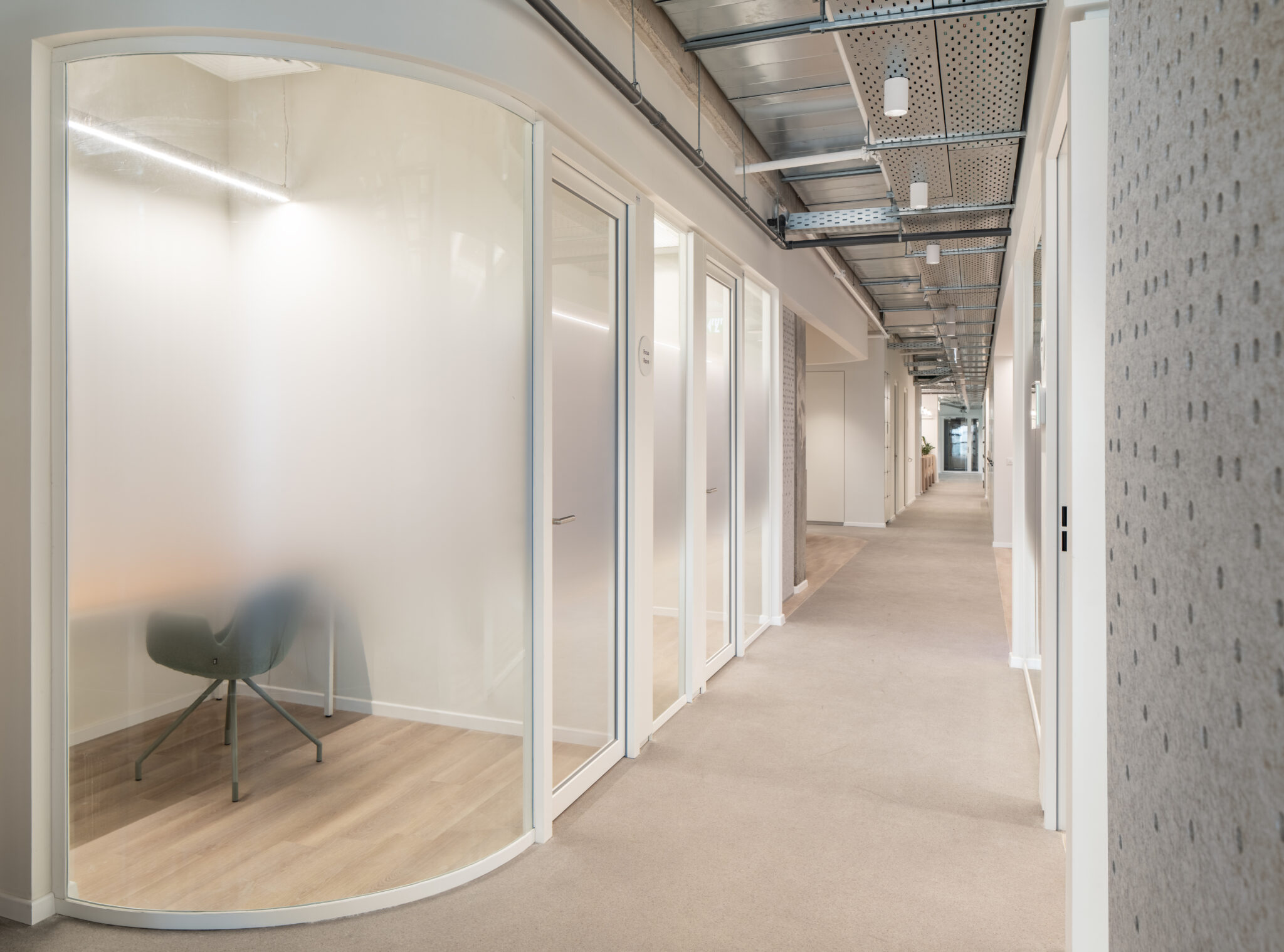 Curved frosted glass office fronts along a corridor with a perforated wall
