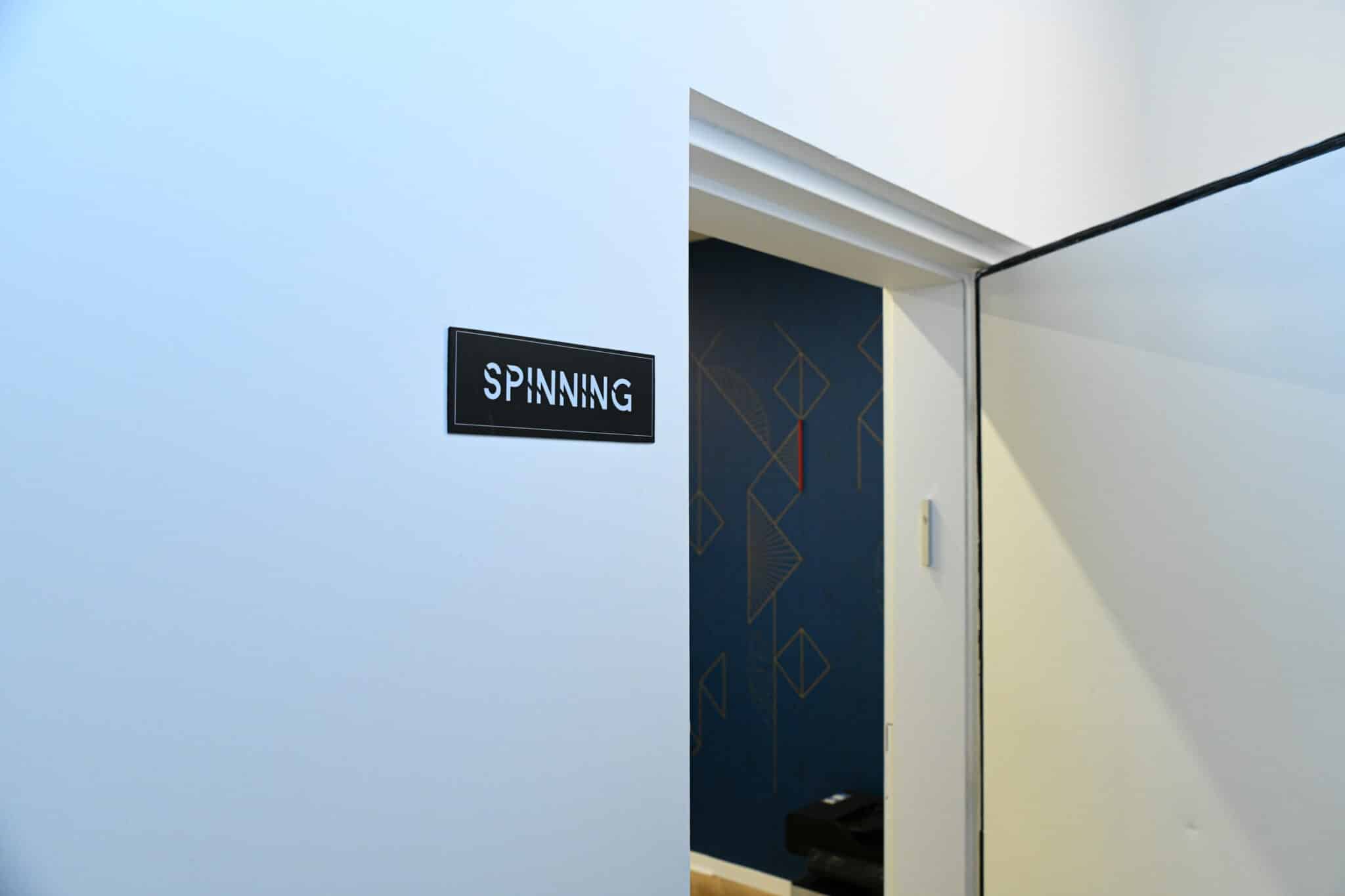 Black SPINNING room sign on a wall beside a doorway