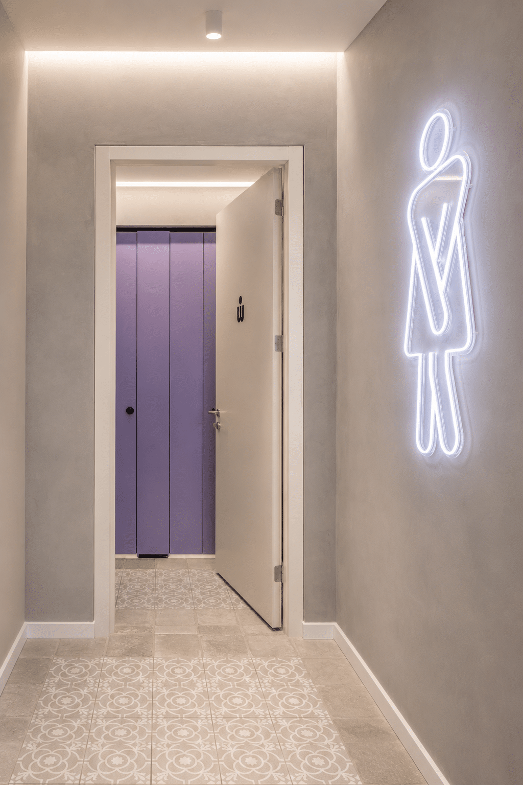 Neon washroom pictogram glowing on a corridor wall
