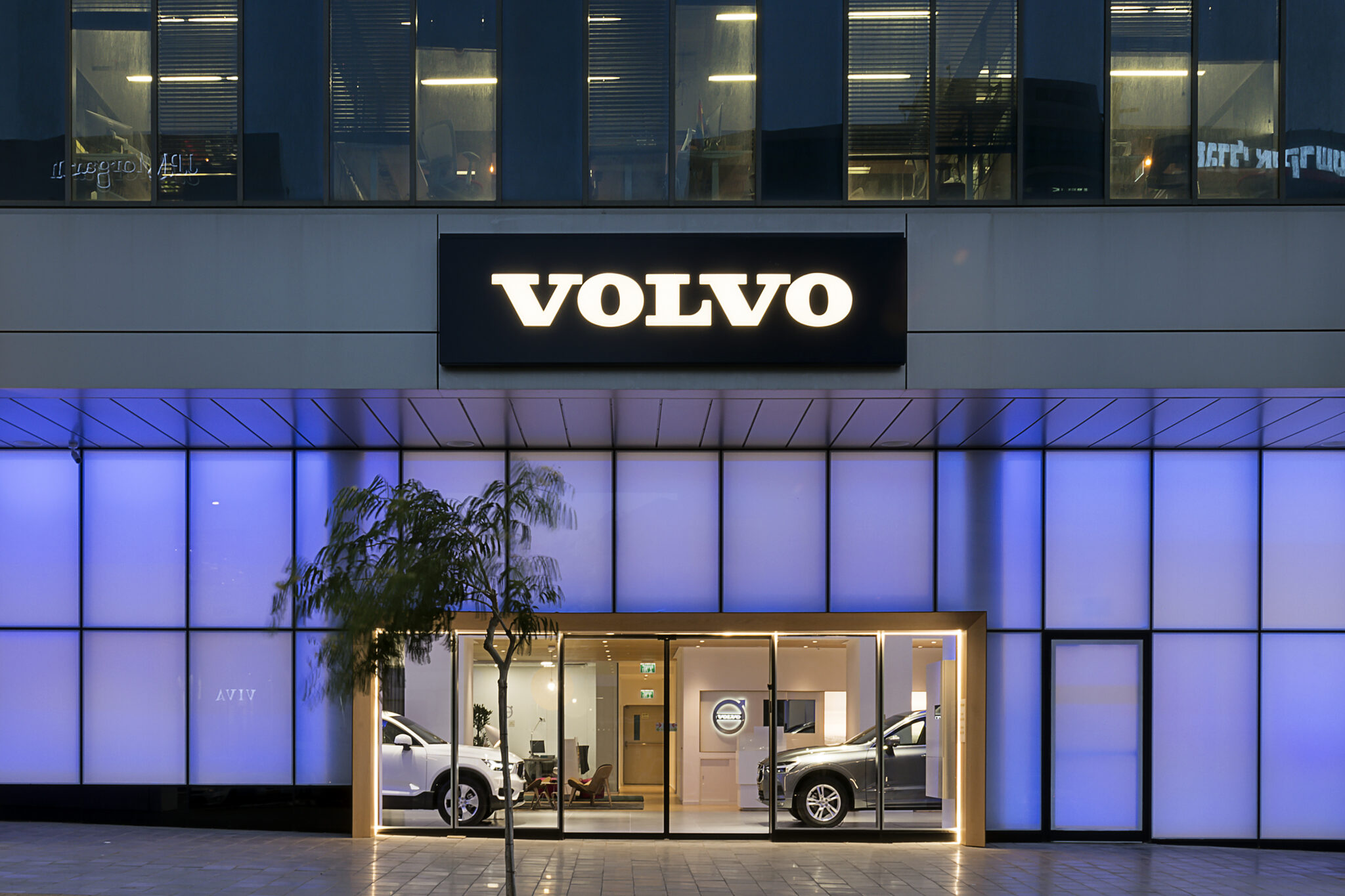 Illuminated VOLVO sign above a lit facade at night