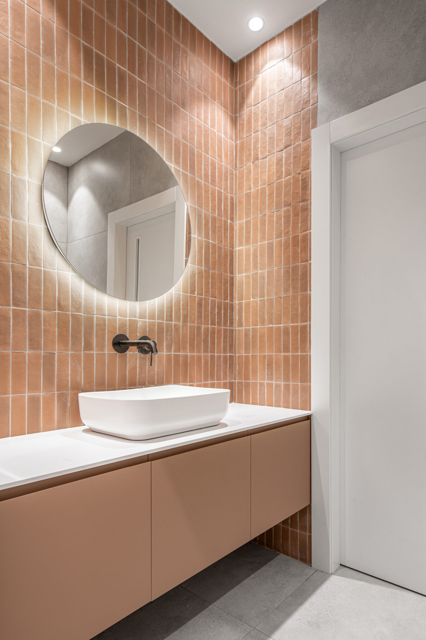 Round backlit mirror on a terracotta tiled washroom wall